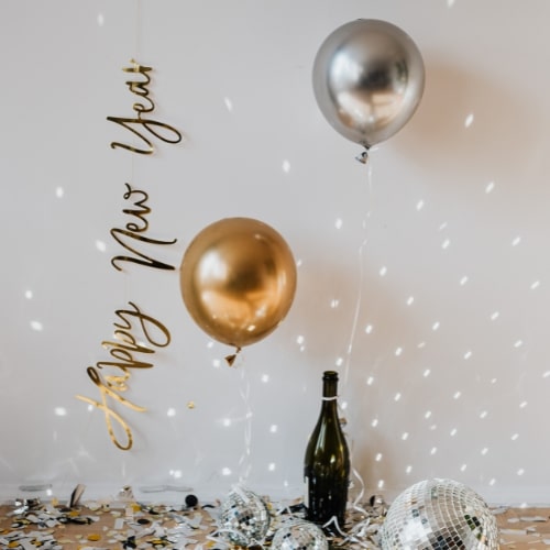 Happy New Year celebration with gold and silver balloons, a champagne bottle, and festive decorations.